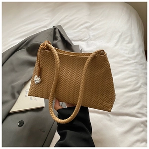 Detail of a brown woven shoulder bag featuring a silver heart pendant on a soft fabric