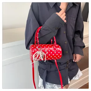 Détail d'un sac à main cylindrique rouge à pois blancs avec pendentif nœud en perles