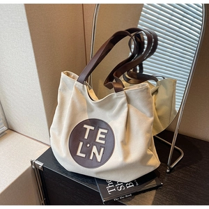 Close-up of cream canvas tote bag with brown leather strap and stylish circular logo patch