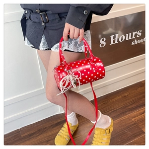 Détail du sac cylindrique rouge à pois avec breloque nœud perlé et finition vernie