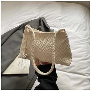 Detailed close-up of beige woven texture and silver heart pendant on a shoulder bag