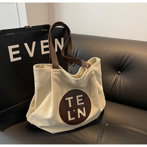 Detailed macro view of large canvas tote bag with circular leather logo and sturdy handles