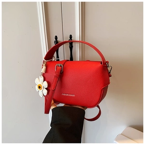 Macro shot of red litchi grain leather texture and white daisy charm on a crossbody bag
