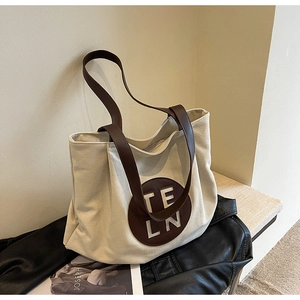 Close-up of beige canvas tote bag with brown leather strap and circular brand logo detail