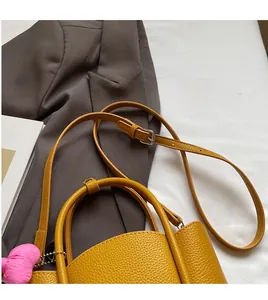 Close-up of ginger yellow litchi grain leather bucket bag with a pink heart pendant