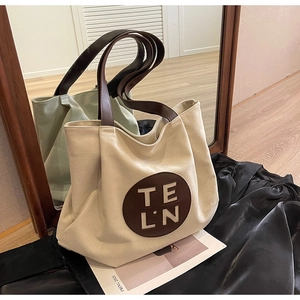 Detail of canvas tote bag with brown leather handles and circular logo on a mirrored floor