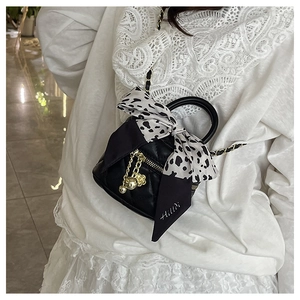 Detail of black quilted mini bag with golden chain and cow print silk scarf bow detail