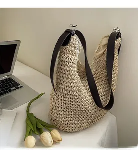 Close-up of woven straw hobo bag with dark brown leather strap and metal buckle detail