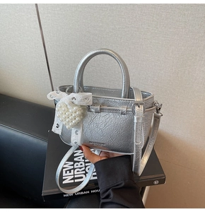 Detail der silbernen Metallic-Eimertasche mit Perlenanhänger und Spitzenschleife