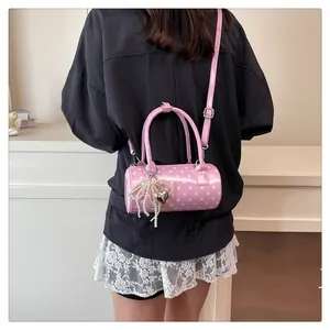 Sac cylindrique rose à pois avec breloques en perles porté par un mannequin en intérieur