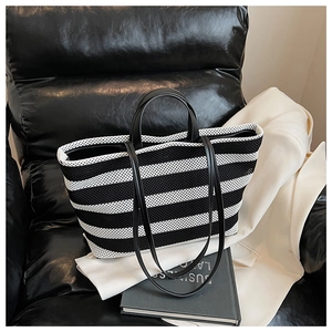 Vue détaillée du sac cabas en maille rayée avec anses en cuir noir sur canapé