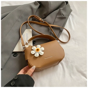 Close-up of brown litchi pattern leather crossbody bag with white daisy charm accessory