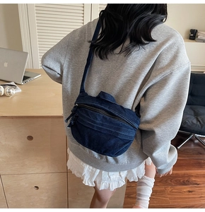 Deep blue denim crossbody bag shown on model with wide strap and zipper detail