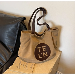Detailed close-up of khaki canvas tote bag with brown leather handles and logo on a sofa