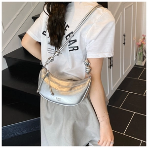 Détail du sac à bandoulière argenté en forme de croissant avec nœuds sur la lanière
