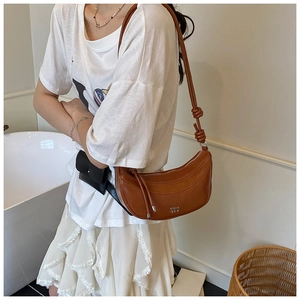 Détail d'un sac demi-lune en cuir souple caramel avec bandoulière nouée et logo en métal