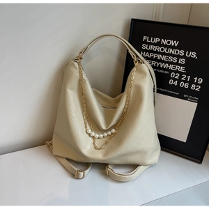 Detail of cream leather tote showing golden chain with pearls on marble surface