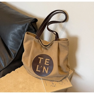 Detail of canvas tote bag with brown leather handles and circular logo patch on stone surface