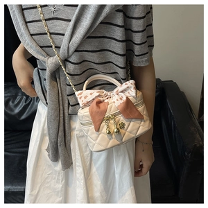 Detail of beige quilted mini bag featuring golden chain and pink floral bow scarf