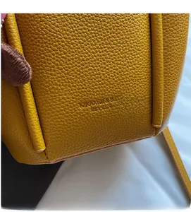 Close-up of yellow lychee grain leather bucket bag with logo and brown plush charm