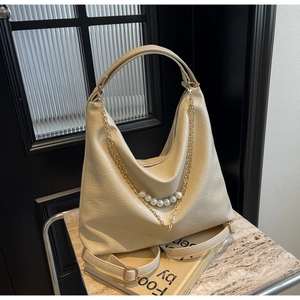 Detail of a creamy white hobo bag with detachable strap and pearl gold chain ornament