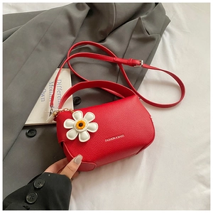 Detail of red lychee textured handbag featuring daisy charm and adjustable shoulder strap