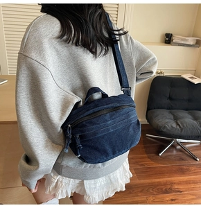 Detailed macro view of dark blue denim crescent shoulder bag with zippers and handle