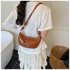 Détail du sac demi-lune en cuir marron avec bandoulière nouée et logo métallique