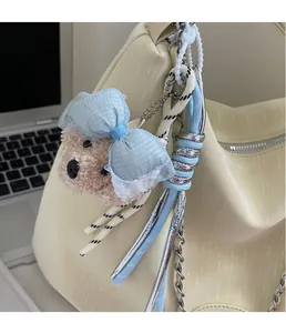 Close-up of a pink plush poodle charm with a blue bow on a beige leather tote bag