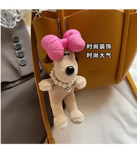 Detail of plush dog charm with pink bow and pearl necklace hanging on a leather bag
