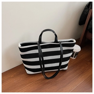 Détail d'un sac cabas à rayures noires et blanches avec doubles anses sur sol en bois