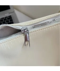 Detailed macro view of a smooth silver zipper pull on an off-white textured tote bag