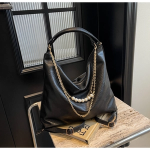 Detail of black hobo bag with elegant gold chains and white pearl embellishments