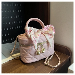 Pink quilted crossbody bag with silk scarf detail and gold chain on wooden surface