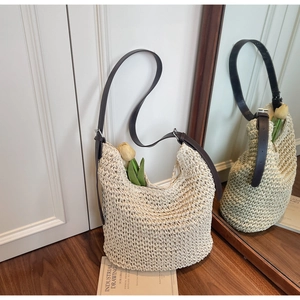 Close-up of woven straw bucket bag featuring dark brown leather strap and silver hardware