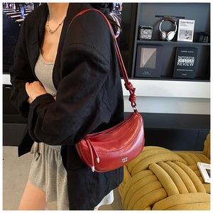 Détail du sac bandoulière rouge en demi-lune avec nœud et logo sur cuir souple