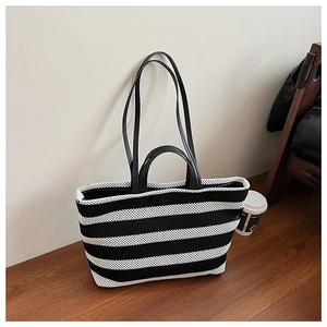 Détail du sac cabas tissé à rayures noires et blanches avec anses en cuir sur parquet