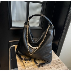 Detail of black pebbled leather hobo bag with thick gold chain and large pearl charms