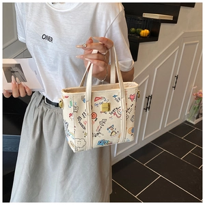 Close-up of a cream tote bag featuring colorful graffiti prints and leather handles