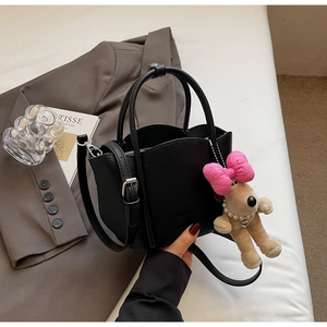 Close-up of black lychee grain leather handbag featuring a cute plush puppy charm