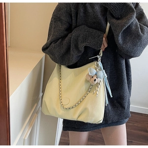 Close-up of textured yellow tote bag featuring a cute teddy bear charm and metal chain strap