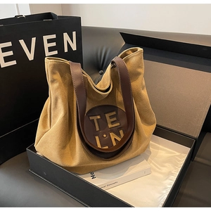 Close-up of khaki canvas tote bag with leather logo patch in a luxury gift box