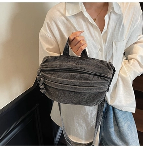 Side view of a vintage grey denim crossbody bag with top handle and wide shoulder strap