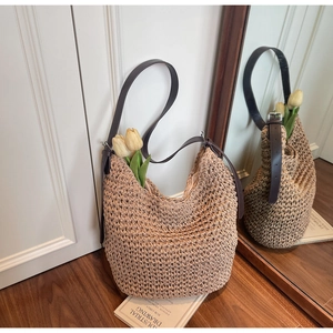 Detail of a large woven straw tote bag with brown leather strap against a mirror