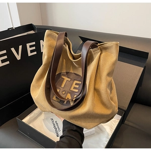 Detail of khaki canvas tote bag with brown leather straps and round logo patch