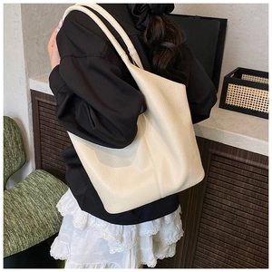 Detail of creamy white lychee grain leather tote bag worn by a model in a warm room