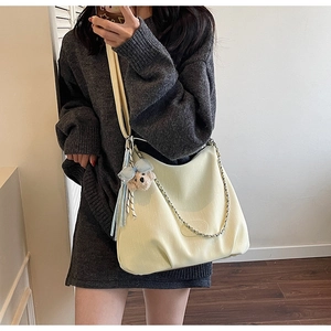 Detail view of cream tote bag featuring vertical texture, silver chain, and bear charm