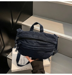 Detailed view of blue denim crossbody bag with double zippers on white book backdrop
