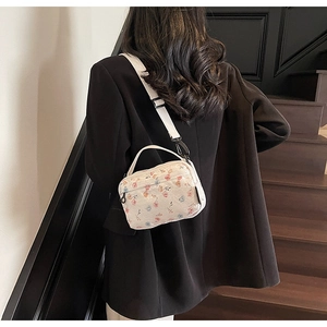 Detail view of floral crossbody bag with canvas texture on a black blazer model