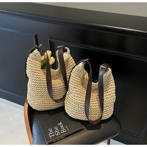 Detail shot of woven straw tote bag with brown leather straps and floral accents
